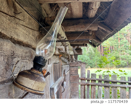A kerosene lamp hangs on the wall of an old log shed. A kerosene lamp hangs on the wall of an old log shed. 117570439