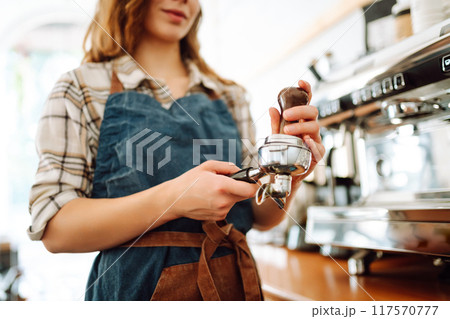 An experienced female bartender prepares a hot drink. Takeaway food. Professional coffee making. 117570777