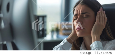Exhausted businesswoman with head in hands sitting with laptop at table in office Exhausted businesswoman with head in hands sitting with laptop at table in office 117572620