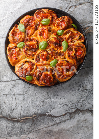 Hot pizza roll with tomatoes, cheese, Italian sausages and basil close-up in baking dish. Vertical top view Hot pizza roll with tomatoes, cheese, Italian sausages and basil close-up in baking dish. Vertical top view 117573165