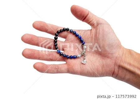 A bracelet made of natural stone beads with a diamond pendant in a man's hand on isolated white background 117573992