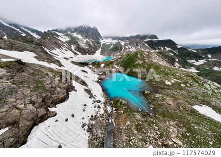 Aerial wide angle view of an alpine lake high in the mountains. Lake surrounded by mountain peaks partially covered with snow 117574029