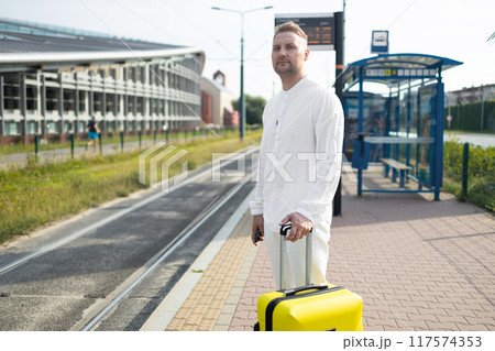 Handsome Tourist Caucasian business man traveler with bag and suitcase sit at public transport bus station waiting with mobile smart phone  117574353