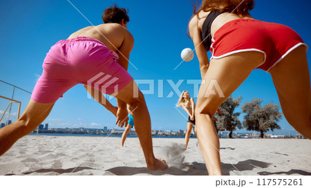 Focused man and woman in colorful beach wear playing beach volleyball under clear blue sky, competing and having fun. 117575261