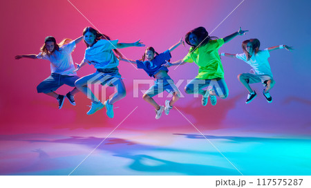 Young girls striking fierce hip hop poses, dancing energetically against gradient pink purple background in neon light Young girls striking fierce hip hop poses, dancing energetically against gradient pink purple background in neon light 117575287