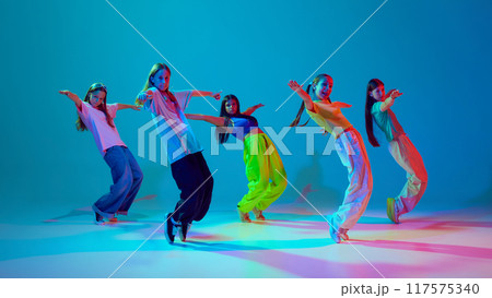 Dynamic synchronized movements of young girls, teens in motion, dancing hip hop against cyan blue background in neon background 117575340