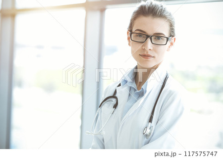 Beautiful woman doctor with stethoscope smiling charmingly and ready to help patients in sunny hospital. Medicine concept 117575747
