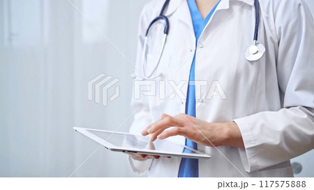 Doctor woman is using digital tablet in clinic. Healthcare professional with a stethoscope operating a touch screen tablet computer while standing straight. Medicine concept Doctor woman is using digital tablet in clinic. Healthcare professional with a stethoscope operating a touch screen tablet computer while standing straight. Medicine concept 117575888
