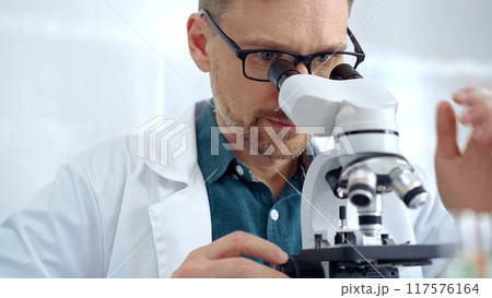 Man scientist with protective glasses using microscope in laboratory. Microbiology science concept 117576164