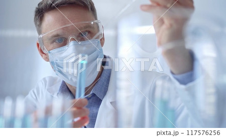 Man with safety glasses and blue mask is working with lab tubes 117576256
