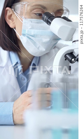 Female scientist using microscope in laboratory. Focus on a woman in lab goggles analyzing samples with a microscope in a scientific setting Female scientist using microscope in laboratory. Focus on a woman in lab goggles analyzing samples with a microscope in a scientific setting 117576264