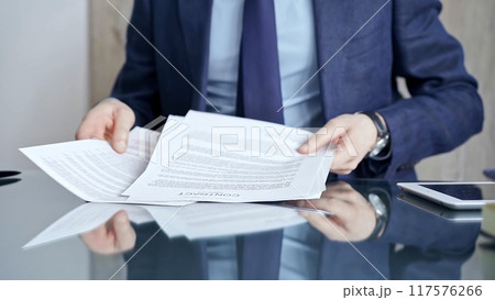 Businessman reviewing documents at office desk. Close-up of a professional man's hands examining paperwork with pen and tablet in sight. Business people concept Businessman reviewing documents at office desk. Close-up of a professional man's hands examining paperwork with pen and tablet in sight. Business people concept 117576266