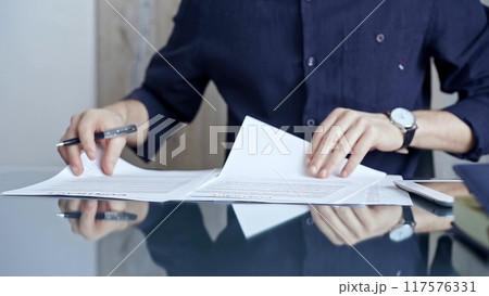 Businessman in dark blue t-shirt is signing contract at desk. Close-up of a male executive signing a legal document on a glass desk. Business people concept 117576331