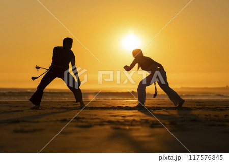 Couple practicing capoeira martial art at sunset on the beach Couple practicing capoeira martial art at sunset on the beach 117576845
