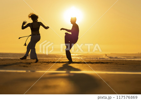 Couple practicing capoeira martial art at sunset on the beach Couple practicing capoeira martial art at sunset on the beach 117576869