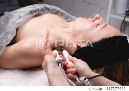 Ultrasonic facial treatment on ultrasound face machine. Woman taking electric lift massage spa salon. Stimulation muscles on professional equipment microcurrent therapy. New methods of rejuvenation Ultrasonic facial treatment on ultrasound face machine. Woman taking electric lift massage spa salon. Stimulation muscles on professional equipment microcurrent therapy. New methods of rejuvenation 117577425