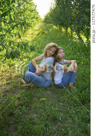 mother and teenage girls with long blond hair spend time together in the sunlit park 117577470
