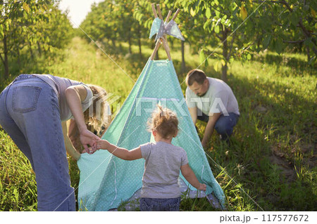 family with toddler playing in wigwam in garden 117577672