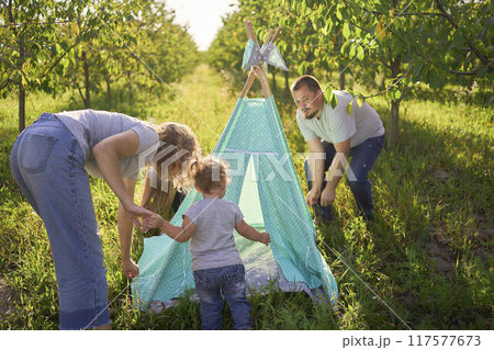 family with toddler playing in wigwam in garden 117577673