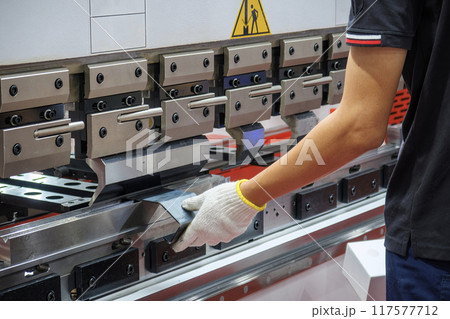 Close up the press brake bending machine operator hold the sheet metal parts with safety glove. Close up the press brake bending machine operator hold the sheet metal parts with safety glove. 117577712