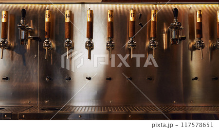 Row of shiny metallic beer taps with numbered wooden handles, mounted on metallic wall. Modern bar equipment 117578651