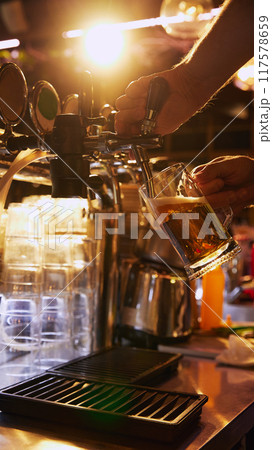 Bartender pouring beer from tap into glass mug, with bar counter and beer taps in the background. Bar aesthetic 117578659