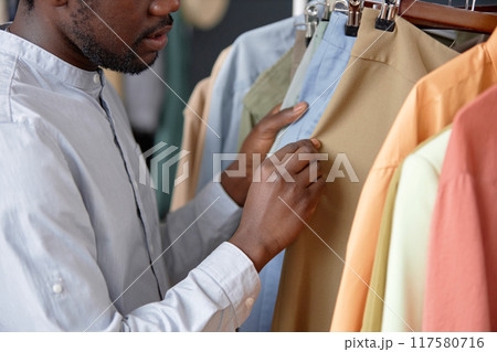 Cropped shot of unrecognizable African American male customer choosing second hand trousers hanging on rack at thrift store Cropped shot of unrecognizable African American male customer choosing second hand trousers hanging on rack at thrift store 117580716