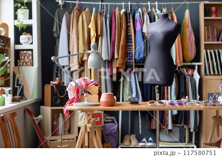 Background shot of workplace of thrift store sales clerk with lamp on retail display table and mannequin next to clothes hanging on rack, copy space Background shot of workplace of thrift store sales clerk with lamp on retail display table and mannequin next to clothes hanging on rack, copy space 117580751