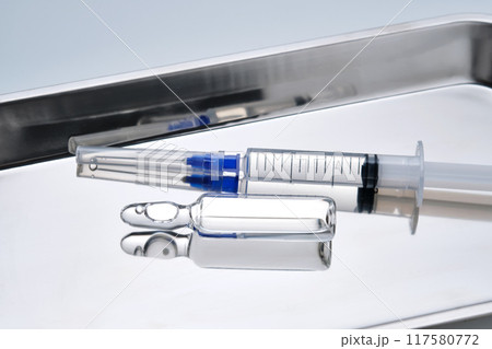 Syringes with needles and an ampoule in a stainless steel medical tray. 117580772