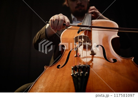 Cropped shot of unrecognizable male cellist performing classical music in dark recording studio with top light, focus on cello 117581097