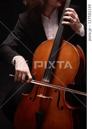 Vertical cropped shot of passionate unrecognizable male musician in black suit playing cello putting on classical music concert in dark studio with dim light Vertical cropped shot of passionate unrecognizable male musician in black suit playing cello putting on classical music concert in dark studio with dim light 117581139