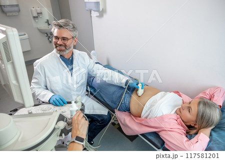 Gray-haired male doctor working on a ultrasonography apparatus Gray-haired male doctor working on a ultrasonography apparatus 117581201