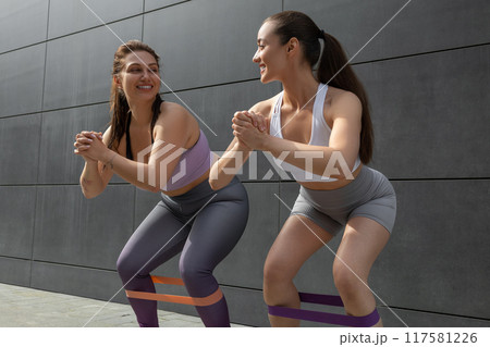 Two smiling young women doing squats with fitness band Two smiling young women doing squats with fitness band 117581226