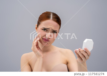 Red-haired lady examining her acne in mirror Red-haired lady examining her acne in mirror 117581274