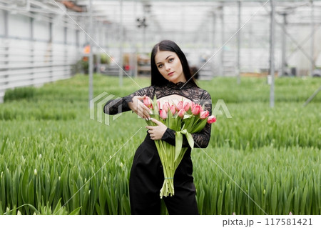 Young woman standing in large greenhouse and holding a blooming tulips in her hands 117581421