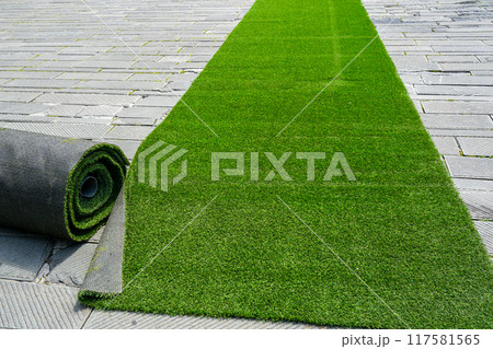 Preparing artificial grass carpet rolls for outdoor event flooring in the town square 117581565