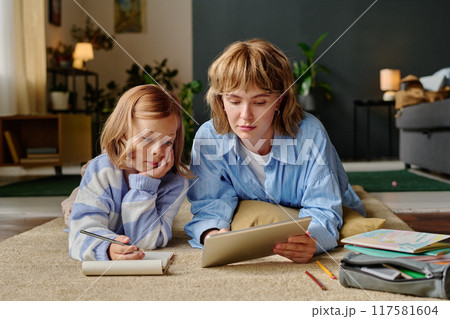 Mom and her daughter laying on soft carpet and taking online course via touchpad Mom and her daughter laying on soft carpet and taking online course via touchpad 117581604