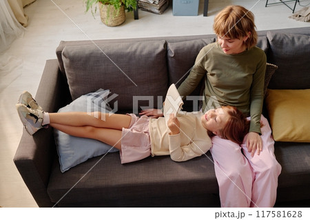 High angle shot of mom dressed in casual outfit sitting next to her happy girl who holding sketchbook High angle shot of mom dressed in casual outfit sitting next to her happy girl who holding sketchbook 117581628