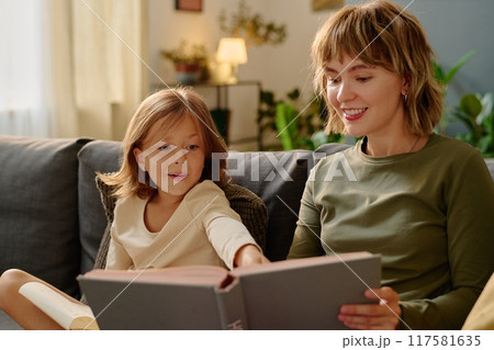 Little girl looking at colorful book illustration while she and her mom reading together Little girl looking at colorful book illustration while she and her mom reading together 117581635