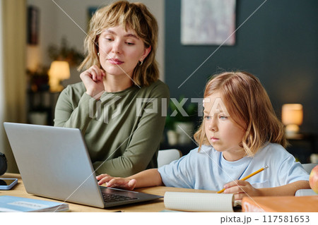 Little girl sitting at desk and learning computer while her mother watching her Little girl sitting at desk and learning computer while her mother watching her 117581653