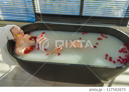 Spa relaxation. Woman lying in bath with red roses petals. Girl relaxing in bathroom at home. Pretty female enjoying taking hot bath. Stress relief. Rest after hard working day Spa relaxation. Woman lying in bath with red roses petals. Girl relaxing in bathroom at home. Pretty female enjoying taking hot bath. Stress relief. Rest after hard working day 117582673