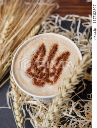 Coffee cup with foam patriotic pattern coat of arms of Ukraine, stencil decor latte mug standing on table with spikelets/ vertical, top view Coffee cup with foam patriotic pattern coat of arms of Ukraine, stencil decor latte mug standing on table with spikelets/ vertical, top view 117582807