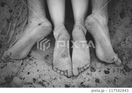 Feet of two persons guy girl lie on dirty beach, men and women heels and toes in sand, top view 117582843