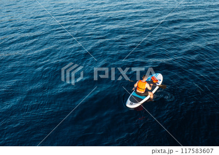Aerial view of man sitting on the SUP surrounded by the breathtaking blue of the azure sea 117583607