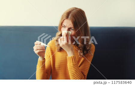 Sick exhausted woman sneezing blow nose measuring checking body temperature thermometer at home 117583640