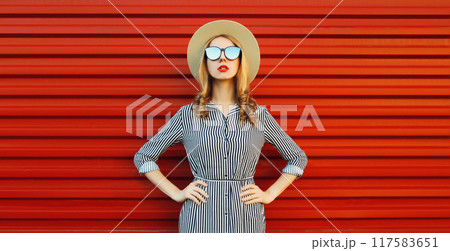 Summer portrait of beautiful stylish young woman, pretty girl posing in hat on red background Summer portrait of beautiful stylish young woman, pretty girl posing in hat on red background 117583651
