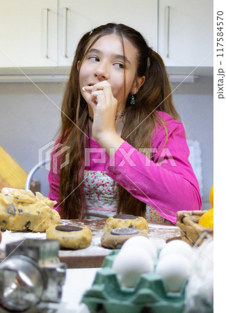 Girl baking cookies in her home kitchen and tasting chocolate with funny face. Girl baking cookies in her home kitchen and tasting chocolate with funny face. 117584570