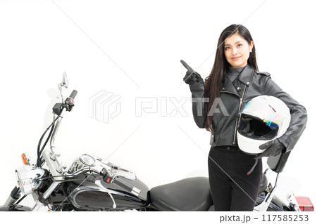 バイクの横に立って、ヘルメットを持って、指差しするバイク女子 バイクの横に立って、ヘルメットを持って、指差しするバイク女子 117585253