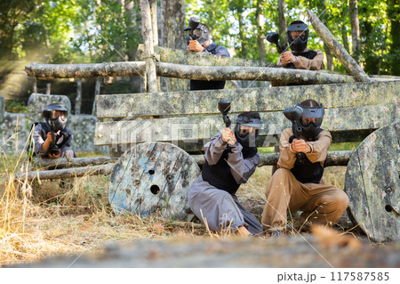 Group of people in full gear playing paintball on shooting range outdoors Group of people in full gear playing paintball on shooting range outdoors 117587585