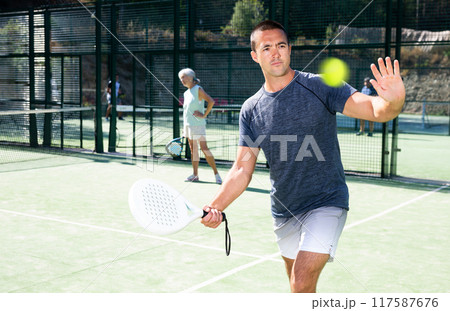 Man swinging racket to hold forehand on open padel tennis court Man swinging racket to hold forehand on open padel tennis court 117587676